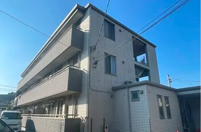 明るいグレー系の外壁をした3階建てアパートの外観。施工前の状態で、全体にやや淡くシンプルな印象を与えている