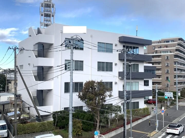 白い外壁を保ちながら黒いバルコニー部分が整えられた4階建てマンション外観。角地に建つ建物が、より引き締まった印象に見える施工後の状態