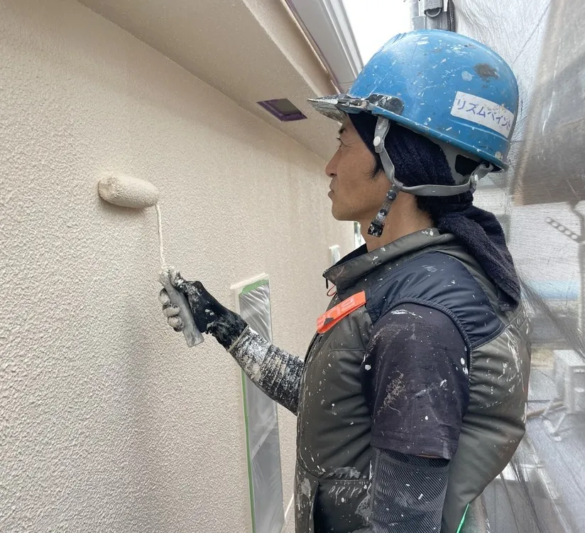 職人がローラーで外壁に白い塗料を塗っている様子